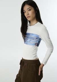 Wit lange mouwen top met een denimprint over de borst; gecombineerd met bruine, gestructureerde broek; gemaakt van zachte stof.
