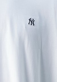 T-shirt bianco in cotone con un piccolo logo ricamato in nero "NY" sul petto. Tessuto morbido, maniche corte e collo a giro.