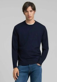Maglione blu navy con scollo rotondo realizzato in tessuto morbido, caratterizzato da maniche lunghe e polsini a coste. Dettaglio logo discreto sul petto.