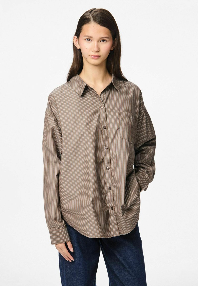 Srajca z gumbi v rjavi barvi z navpičnimi črtami, z enim žepom na prsih, sproščen kroj in dolgimi rokavi. Tkanina se zdi gladka in lahka.