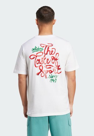 White cotton t-shirt featuring colorful, glossy text on the back: red "The Taste of Sport" and green "since 1949." Classic crew neck design.