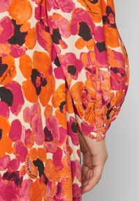 Färgglad tyg med blommönster i nyanser av rosa, orange och svart; har puffärmar med elastiska manschetter och en texturerad yta.