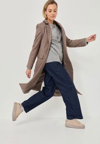 Brown wool blend coat over a gray cardigan, paired with loose blue denim pants and beige platform sneakers, featuring textured fabrics.