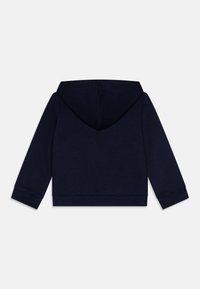 Hanorac cu glugă de culoare bleumarin, cu mâneci lungi, realizat dintr-un material moale, având un buzunar de tip cangur și mansete și tiv din material rib. 
