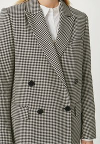 Veste croisée à motif pied-de-poule en noir et blanc avec un revers cranté, dotée de boutons noirs et d'une coupe structurée.