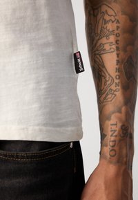 Lysegrå T-shirt med en subtil tekstur, der har et sort mærke på side sømmen. Bæret med mørk denim jeans.