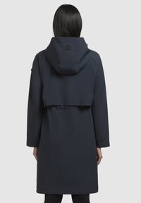 Manteau imperméable bleu marine avec capuche à cordon de serrage et poignets élastiques, présentant une taille cintrée et un design mi-long. Texture lisse, détails minimaux.