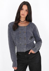 Cardigan blu a maglia tagliata con motivi testurizzati e cinque bottoni decorativi dorati. Presenta maniche lunghe e polsini a coste.