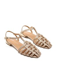 Sandali piatti intrecciati in oro con punta aperta, cinturino slingback e design intrecciato. Interno liscio e tacco basso per il massimo comfort.