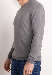 Pull gris à manches longues avec col en V, présentant une texture douce et des poignets et ourlet côtelés ; porté avec un jean bleu.