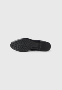 Sola de sapato preto masculino com padrão de tração circular e calcanhar liso, fotografada sobre um fundo branco liso.