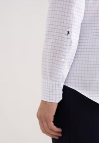 Weißes Hemd mit Knopfleiste und hellblauem Karomuster. Manschette mit floraler Stickerei und zwei Knopfverschlüssen. Glatte Stofftextur.