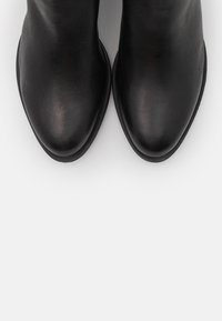 Černé kožené kotníkové boty s hladkou texturou, mandlově tvarovanou špičkou a minimalistickým designem. Mají nízkou, plochou podrážku a žádné viditelné kovové prvky.