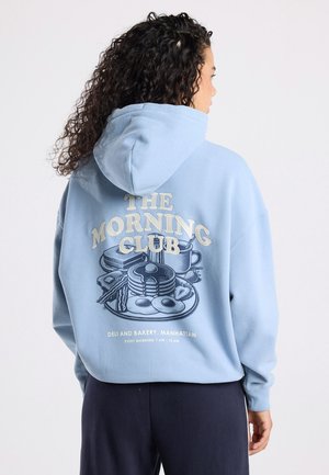 Lichtblauwe hoodie met een grafische print van een ontbijtscène op de achterkant. Bevat tekst en illustraties van voedselitems en een kopje.