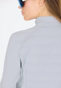 Lys grå cykelsjakke med høj krave og quiltet tekstur. Har sømdetaljer og en tætsiddende pasform. Accentueret af minimal hardware.