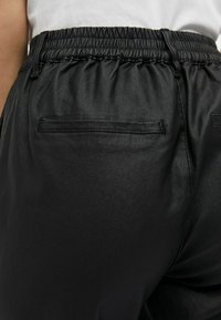 Pantalons noirs en simili cuir avec une taille élastique, une texture lisse et une poche arrière unique avec un bord cousu.