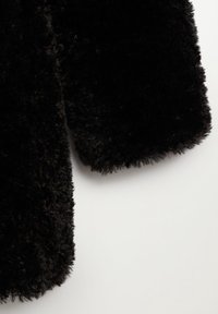 Zwart, donzig buitenstof met een zachte, gestructureerde oppervlakte en een afgeronde rand. Het materiaal lijkt knus en dicht, biedt warmte.