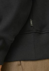 Felpa nera con vita e polsini a costine, texture morbida, caratterizzata da un piccolo etichetta in tessuto sul lato e una cucitura a contrasto.