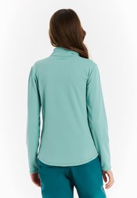 Dlhý rukáv top v svetlo akvamarínovej farbe, vyrobený z hladkej, elastickej látky. Obsahuje zipsový výstrih a diskrétne logo blízko goliera.