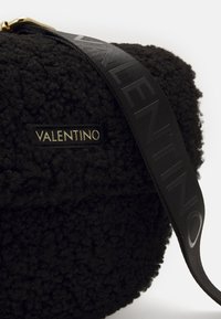 Black textured bag with a fluffy material, featuring a gold logo plaque and a black strap with gray "VALENTINO" lettering.