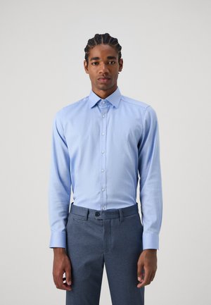 Light blue long-sleeve shirt with a button-down collar, smooth texture, and fitted design. Paired with gray patterned trousers.