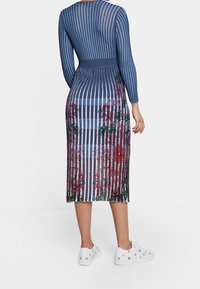 Stickad klänning med vertikala marinblå och ljusblå ränder, med blommönster vid kanten. Bärs med vita sneakers, accentuerad med detaljer i metall.