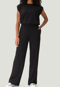 Completo due pezzi nero e texturizzato, caratterizzato da una maglietta a maniche corte e pantaloni a gamba larga, con tasche laterali. Scarpe argentate completano il look.