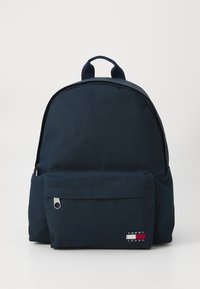 Marinblå tygryggsäck med rundad form, framficka med dragkedja och en liten logopatch. Har ett handtag på toppen och justerbara remmar.