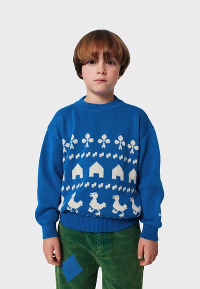 Modrá pletená mikina s bielymi vzormi kvetov, domov a kurčiat; okrúhly výstrih; rebrované manžety; nosené s zelenými kordovým nohavicami.