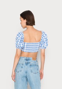 Top cropped em padrão de gingham azul e branco, com mangas bufantes e decote quadrado, combinado com jeans de cintura alta de denim azul claro.