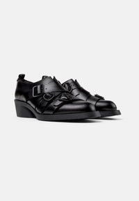 Zapatos de cuero negro con un upper texturizado, presentan correas decorativas y hebillas, puntera redondeada y un tacón bajo y sólido.