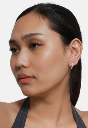 Boucle d'oreille en argent avec une finition lisse, présentant un design élancé. Le modèle a une expression neutre, mettant en valeur le bijou de manière claire.