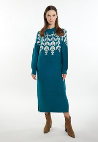 Rochie tricotată în nuanță de teal, cu mâneci lungi, având motive albe cu frunze la piept. Fante laterale și textură moale vizibile.