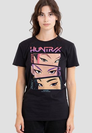 Black cotton t-shirt featuring a graphic print of three stylized faces with bold lines and vibrant eye makeup; text includes "HUNTRAX" and character names.