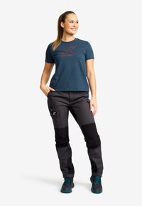 Teal short-sleeve shirt with red logo, paired with black cargo pants featuring knee patches and side pockets, worn with gray and teal shoes.