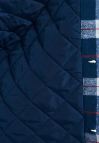Marineblå quiltestof med diamantmønster og glat overflade, parret med et ternet flannel-for i blå, rød og hvid.