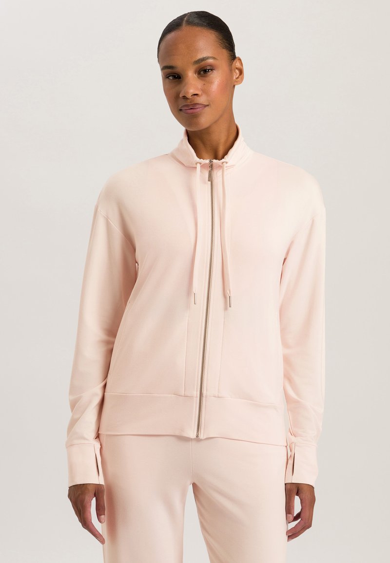 Giacca zip-up rosa chiaro realizzata in tessuto morbido, con colletto alto, maniche lunghe e cuciture laterali sottili. Texture liscia su tutta la superficie.