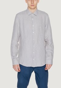 Camicia a righe grigio chiaro con colletto, maniche lunghe e bottoni bianchi. Indossata con pantaloni blu, dal fit casual.