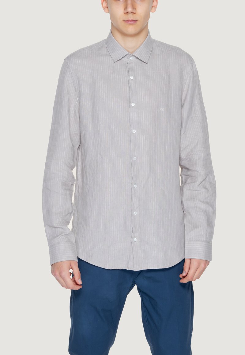 Camicia a righe grigio chiaro con colletto, maniche lunghe e bottoni bianchi. Indossata con pantaloni blu, dal fit casual.