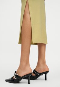 Πόδια με ανοιχτοπράσινη φούστα με πλαϊνή σχισμή και μαύρες μυτερές γόβες με τακούνι, διακοσμημένες με πόρπη και καρφιά.