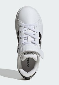 Bijela sportska cipela s crnim prugama, izrađena od sintetičke kože, s teksturiranim jezikom i vezicama s čičak-trakom.