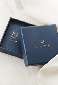 Navyblaues Kästchen mit mattem Finish, mit goldener Schrift: "SEHEN SIE DAS UNSICHTBARE" und "VIOLET HAMDEN," mit einem Akzent in Form eines Halbmonds innen.