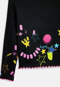 Schwarzes Stricktop mit bunten Stern- und abstrakten Designs in Pink, Gelb und Blau. Die Ränder sind rüschend mit einem pinken Saum.