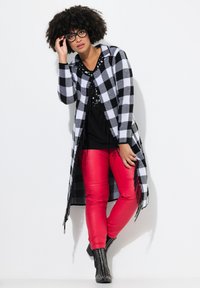 Lang zwart-wit geblokte cardigan met franjes, gedragen over een zwarte top en rode synthetische leren broek. Zwarte, gespikkelde enkellaarzen.