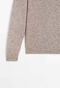 Hnědý pletený svetr s dlouhými rukávy, který se vyznačuje jemnou texturou a žebrovaným lemem. Materiál má jemný vzor a lehký design.