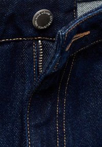 Tmavě modrá džínovina s viditelným prošitím, stříbrný zip a kovový knoflík s vyrytým nápisem "WNG DENIM".