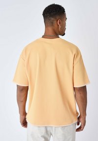Camicia a maniche corte, di un leggero arancione testurizzato con cuciture bianche in contrasto, caratterizzata da una vestibilità rilassata e scollatura rotonda.