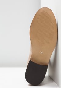 Semelle d'une chaussure beige avec une adhérence texturée et un talon noir, marquée de la taille 37, présentée en angle sur un fond blanc avec des coins.