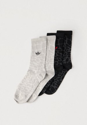 Tri para nogavic: ena svetlo siva z vzorcem teksture in črnim logotipom ter dve črni z enakim vzorcem, pri čemer ima ena rdeč logotip.