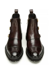 Botas de tobillo de cuero marrón con un acabado suave, punta redondeada, cremalleras laterales y tres detalles en tono dorado en el lado exterior.